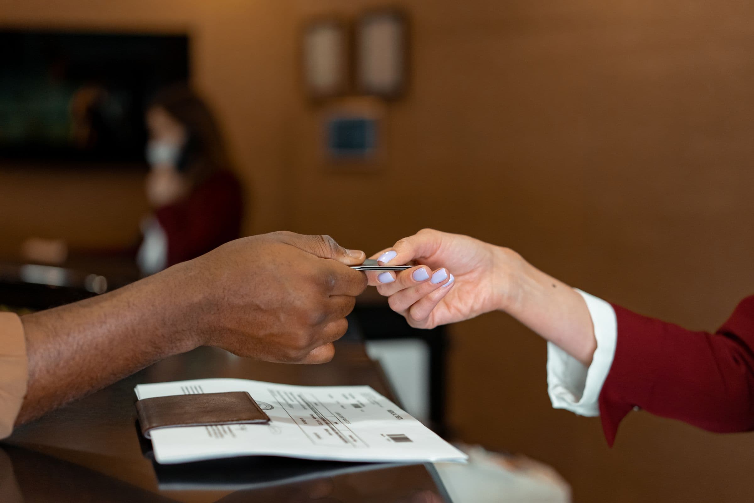 At a hotel front desk, a guest hands a card across the counter to the receptionist.