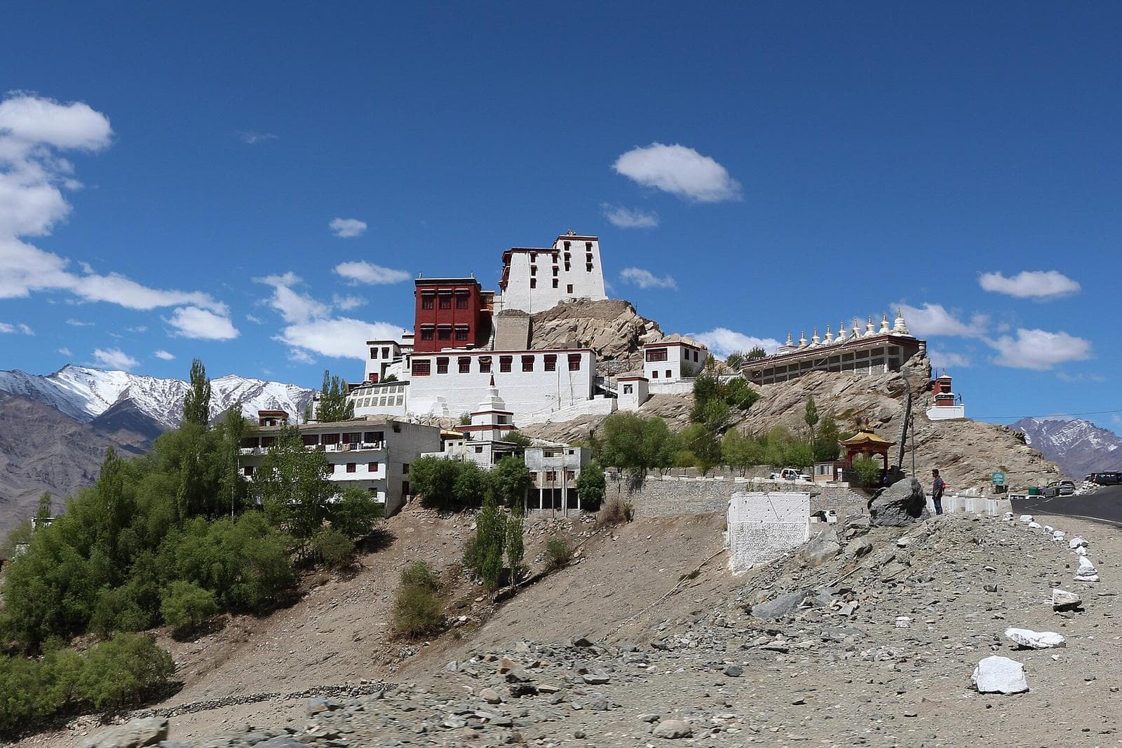 Thiksey Monastery rising in white tiers up its hill, with snow peaks behind.