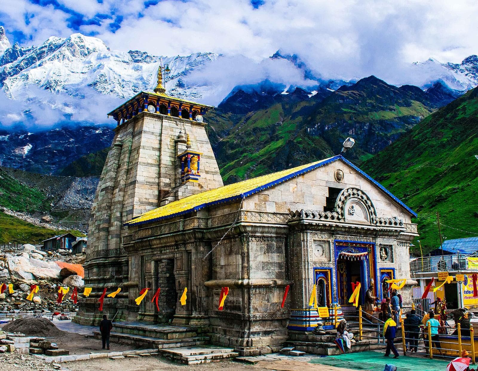 The stone Kedarnath temple, with green slopes and snow peaks behind it.