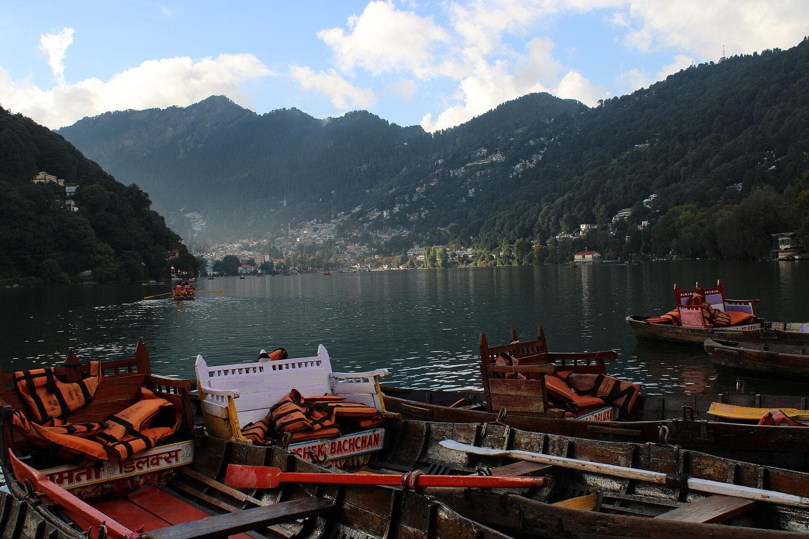Rowing boats moored on Naini Lake, with the town of Nainital on the hills around it.